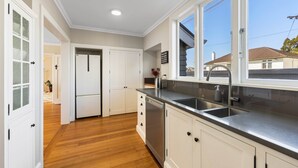 Una cocina con armarios blancos, un lavamanos de acero inoxidable y un ventanal que proporciona luz natural.