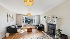 Una sala de estar moderna con chimenea, dos sofás de cuero negro, una mesa de centro de madera y un ventanal con cortinas.