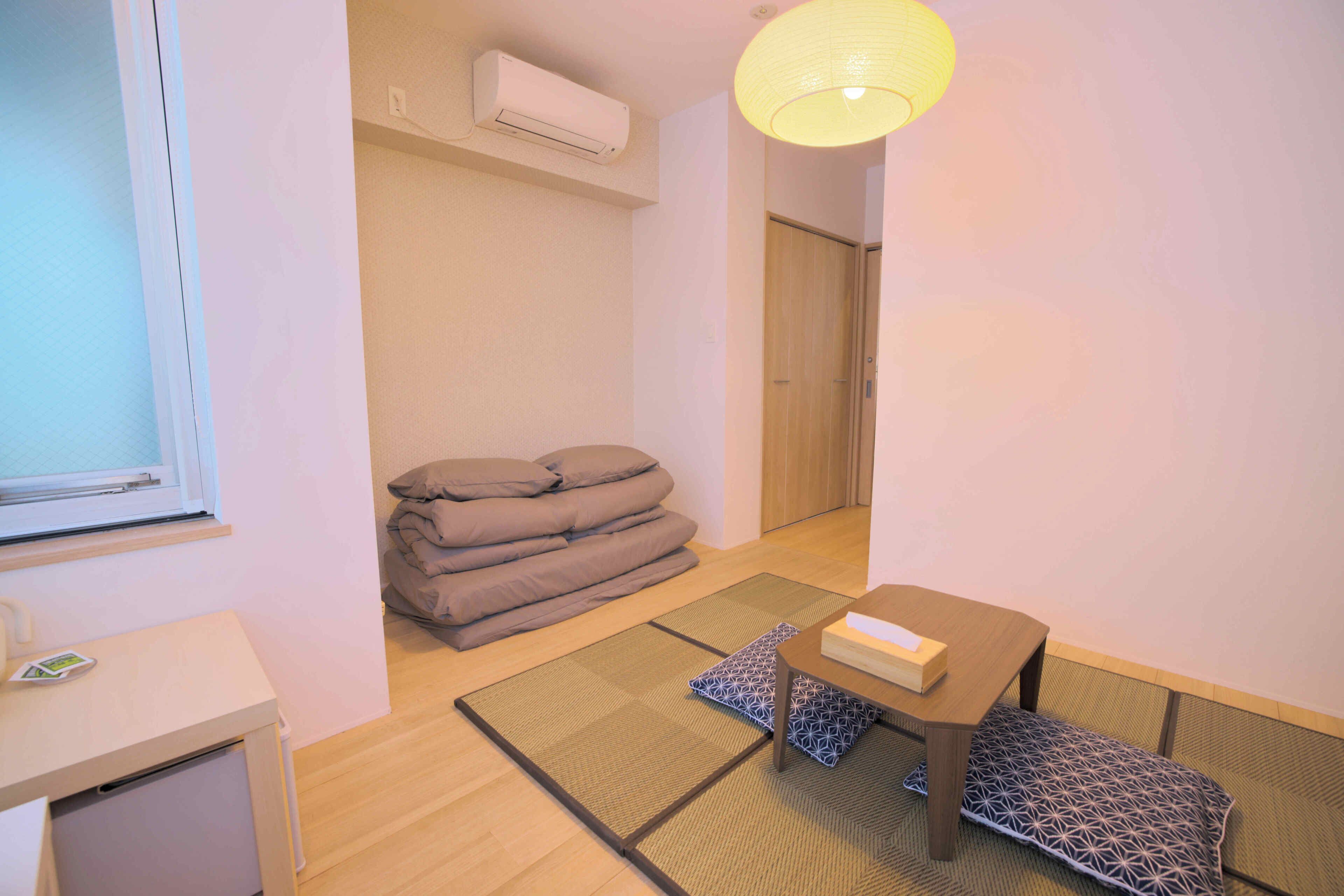 A room with tatami mats, a low table with a box, and a stack of pillows.