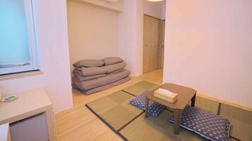 A room with tatami mats, a low table with a box, and a stack of pillows.