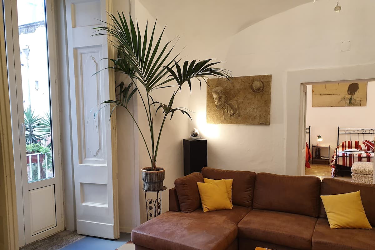 Una sala de estar con un sofá marrón, cojines amarillos, una planta en maceta y un cuadro en la pared.
