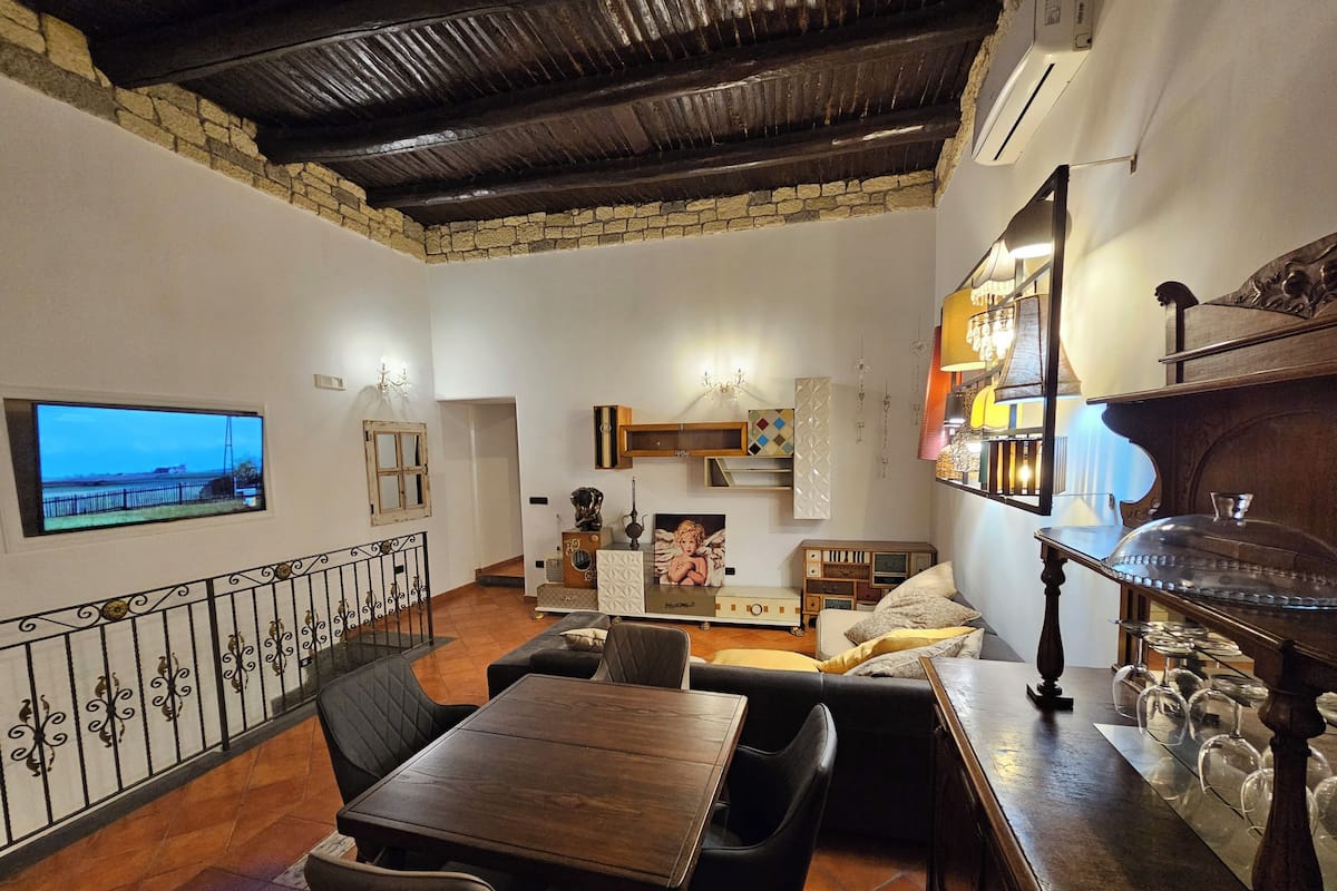 Una sala de estar acogedora con una mesa y sillas de madera, un televisor y un estante decorativo con cristalería.