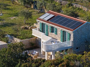 A stone house with a red-tiled roof, green shutters, and solar panels.