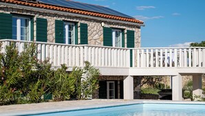 A poolside view of a building with a stone facade, green shutters, and a white balcony railing. - Villa Maslina: Rustic villa in an olive grove facing a bird sanctuary  (Kolan)