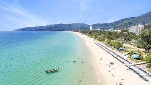 Una spiaggia con acqua cristallina turchese, una fila di ombrelloni e una barca in acqua.