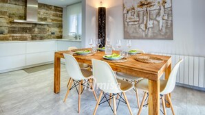 A modern dining area with a wooden table set for four, white chairs, and a large abstract painting on the wall.