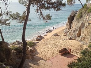 Une plage côtière bordée d’une falaise rocheuse, d’une plage de sable et d’une petite construction avec des marches descendant vers la plage.