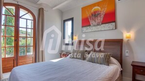 A bedroom with a large bed, a window with curtains, a painting on the wall, and a ceiling fan.