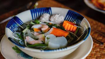 Un tazón de sopa con camarones y verduras sobre una estera tejida.