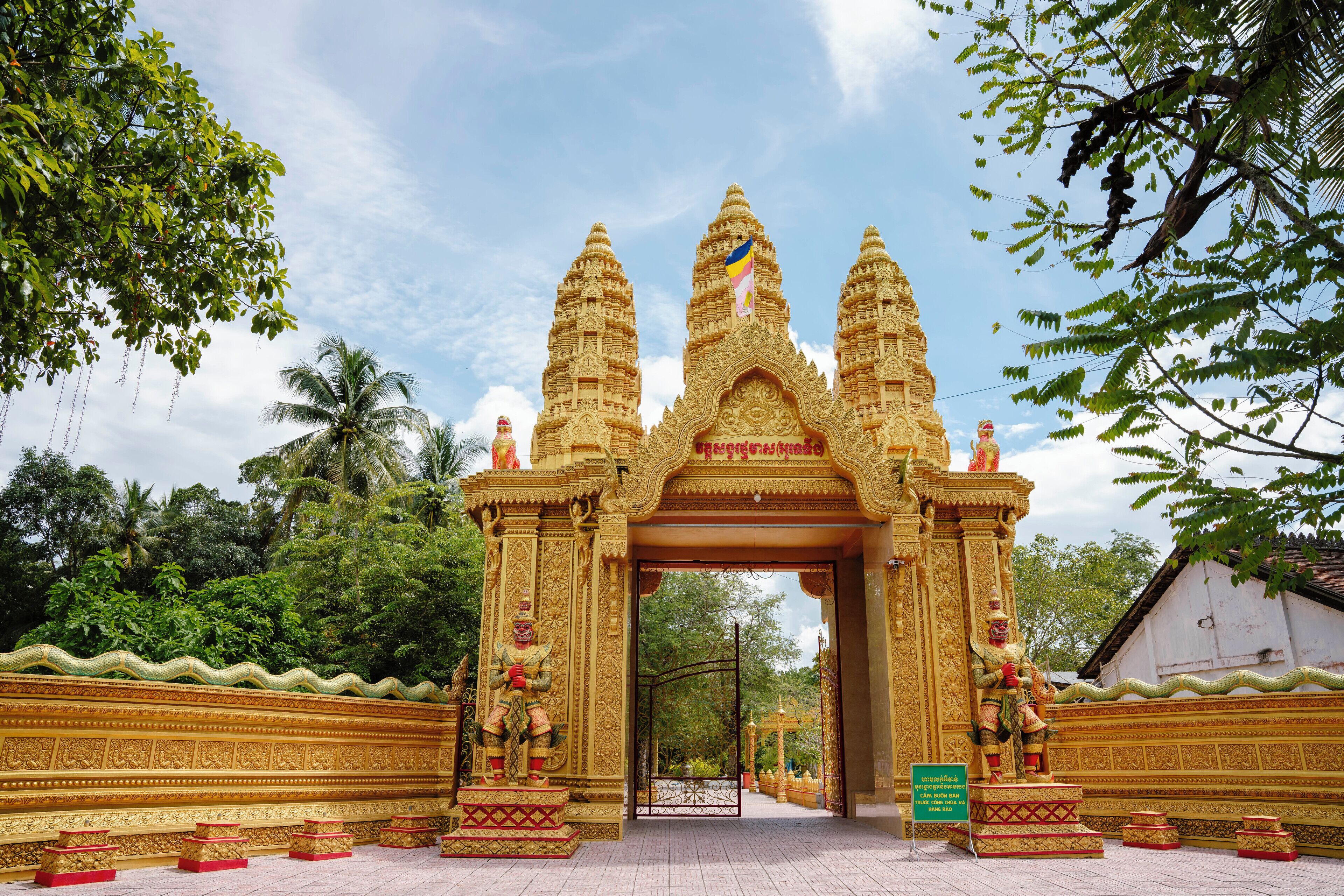 A temple entrance with ornate golden architecture, a central deity statue, and a signboard.