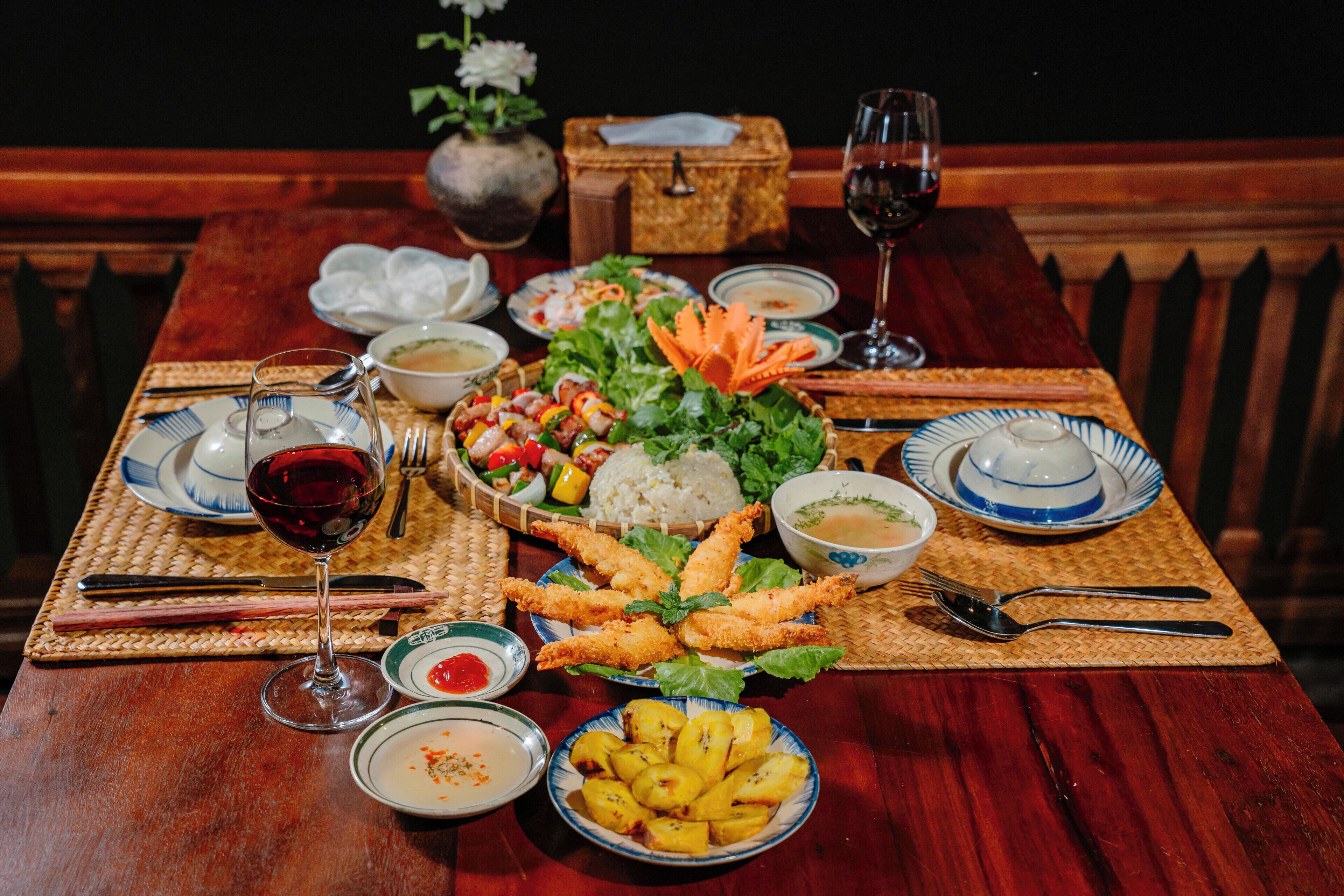 A dining table set with various dishes, including rice, shrimp, and a salad, along with wine glasses and cutlery.