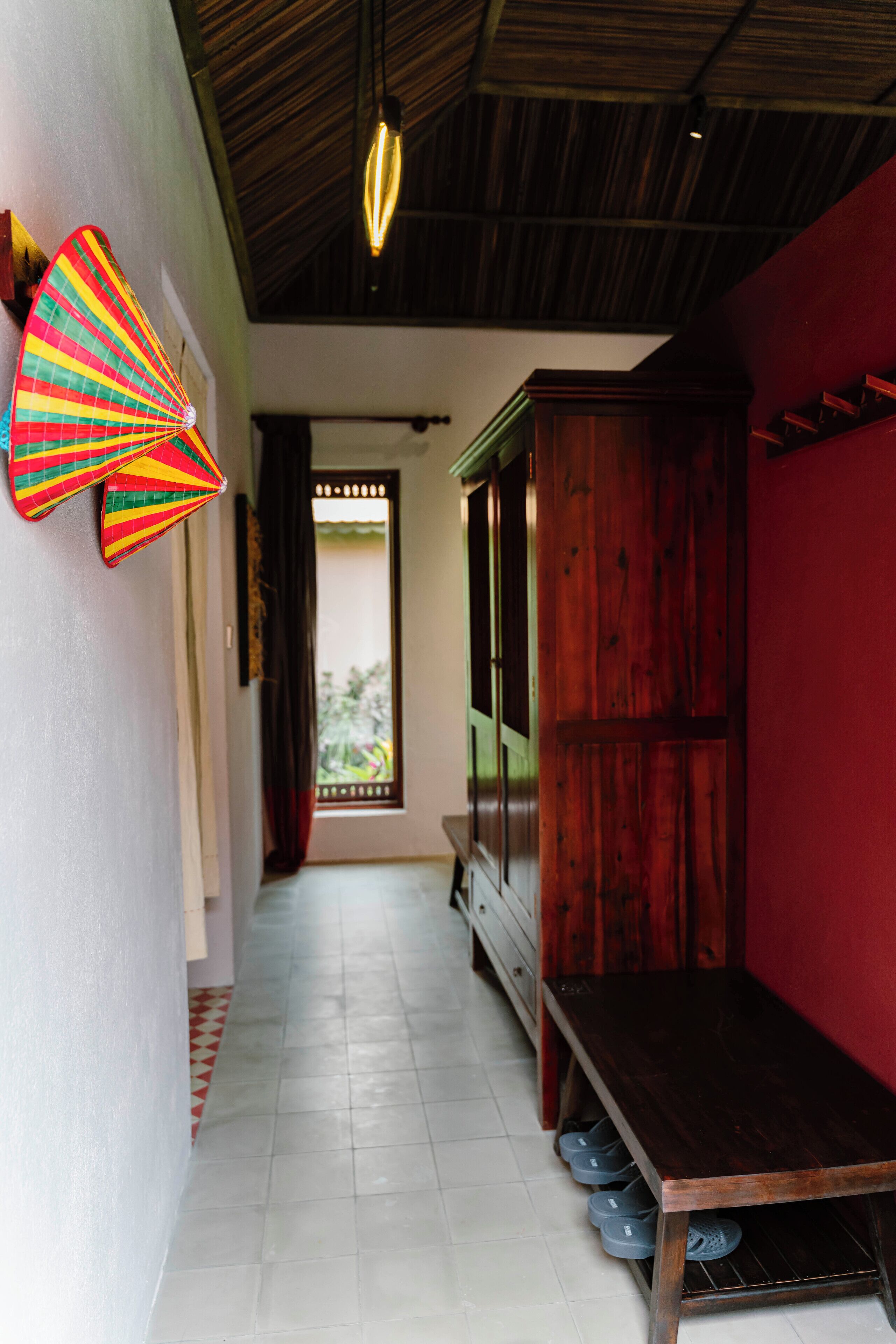 A hallway with a wooden bench, a fan, and a window with curtains.