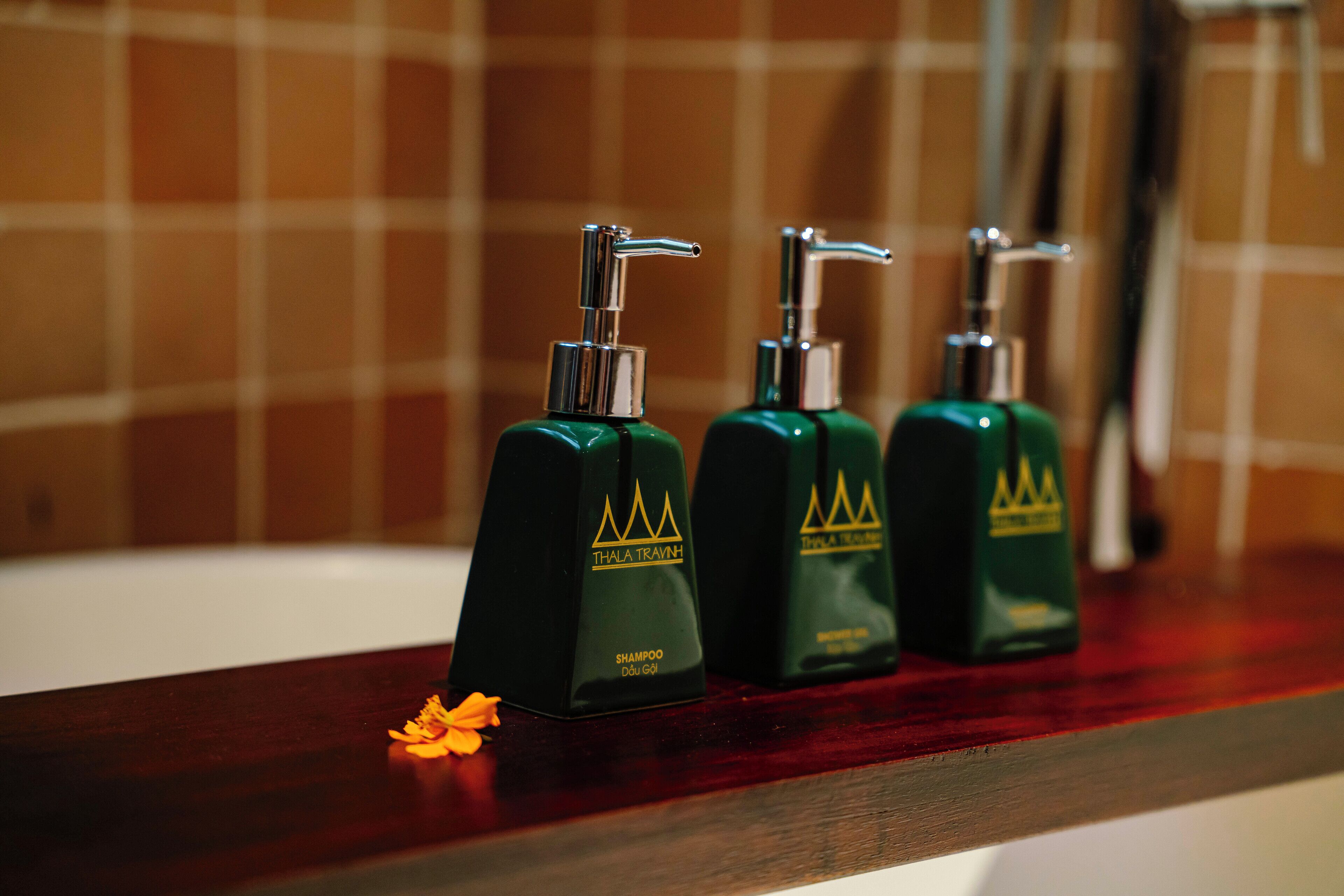 Three green shampoo bottles with silver pumps on a wooden shelf in a bathroom.