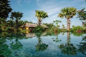 A clear pool with reflections of palm trees and a thatched-roof hut. - Thala Tra Vinh (Cầu Kè)