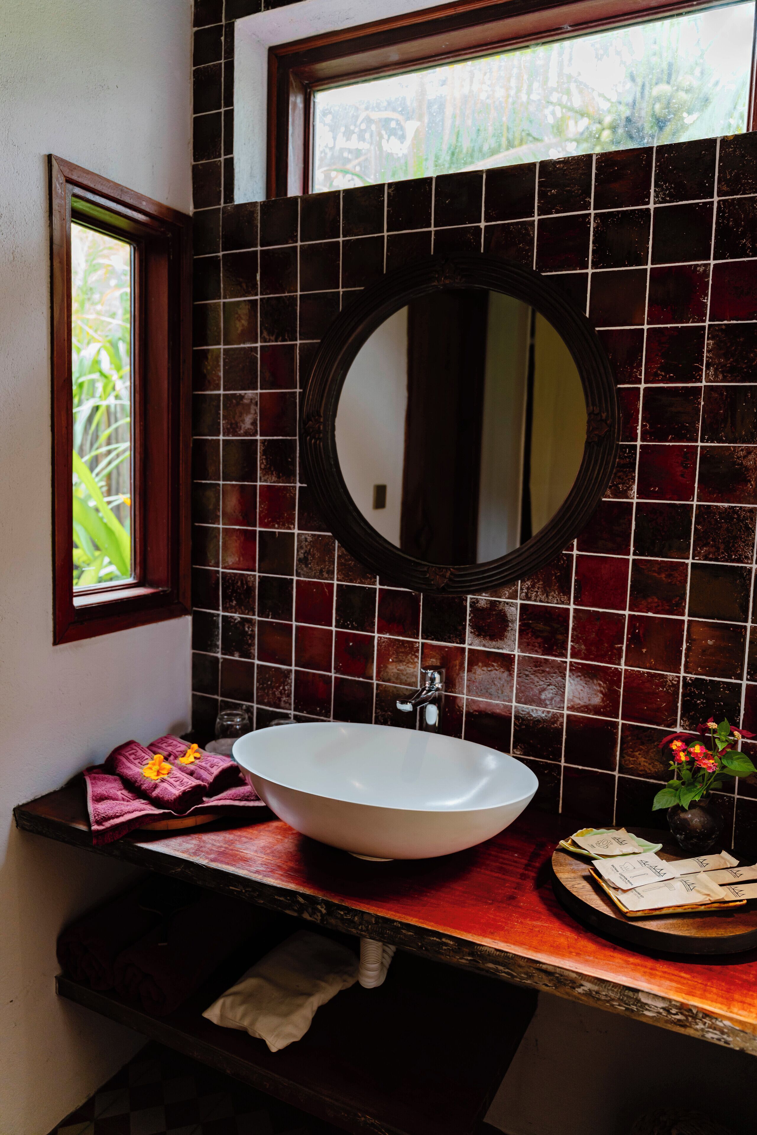 Een badkamer met een wit wastafelmeubel, een spiegel en een raam met uitzicht op groen.