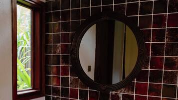 Een badkamer met een wit wastafelmeubel, een spiegel en een raam met uitzicht op groen.
