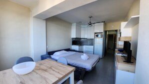 Ett kompakt hotellrum med en säng, ett litet pentry, en matplats med bord och stolar samt en mikrovågsugn.