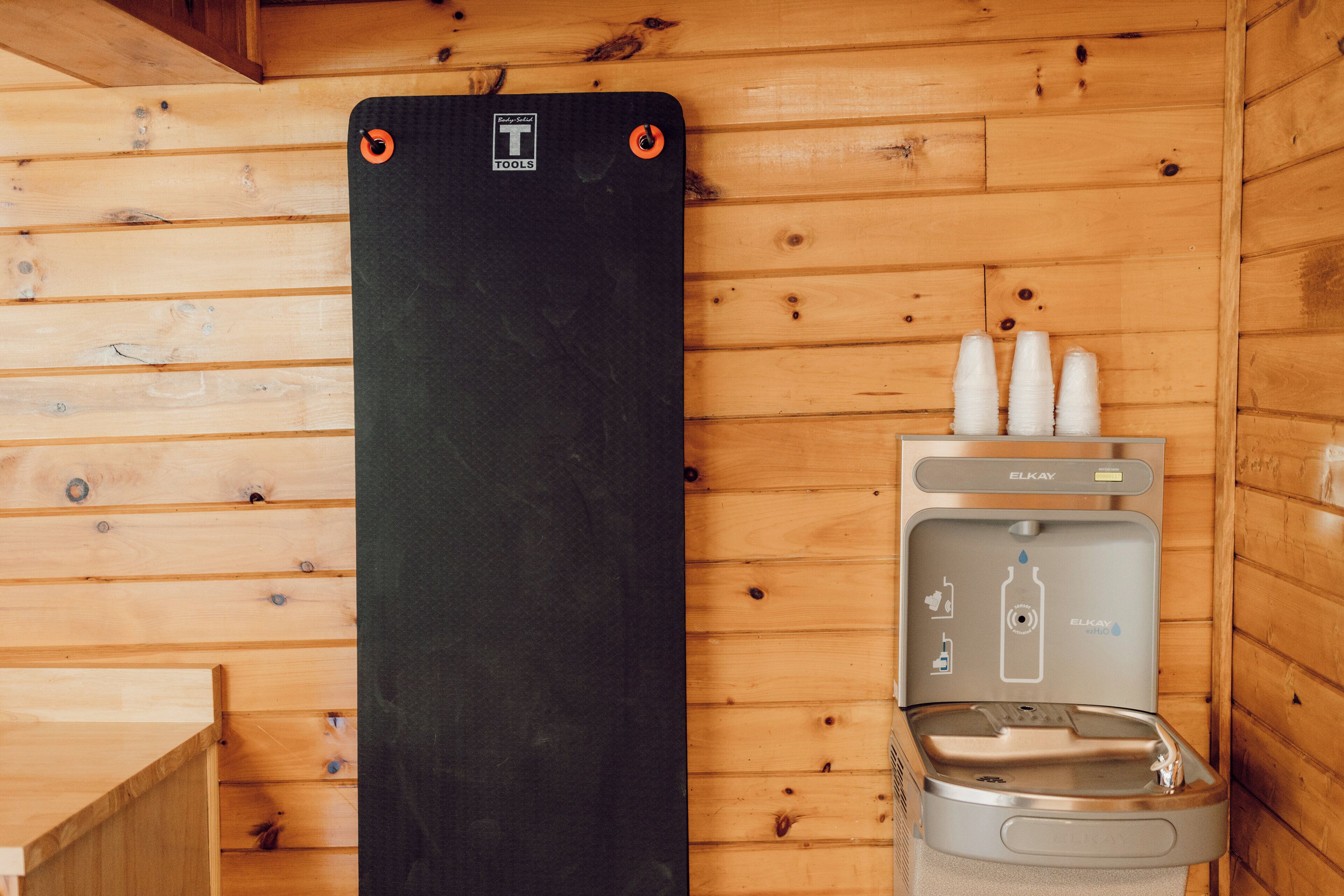 Un sauna équipé d’un tapis noir, d’un distributeur d’eau et de trois tasses blanches.