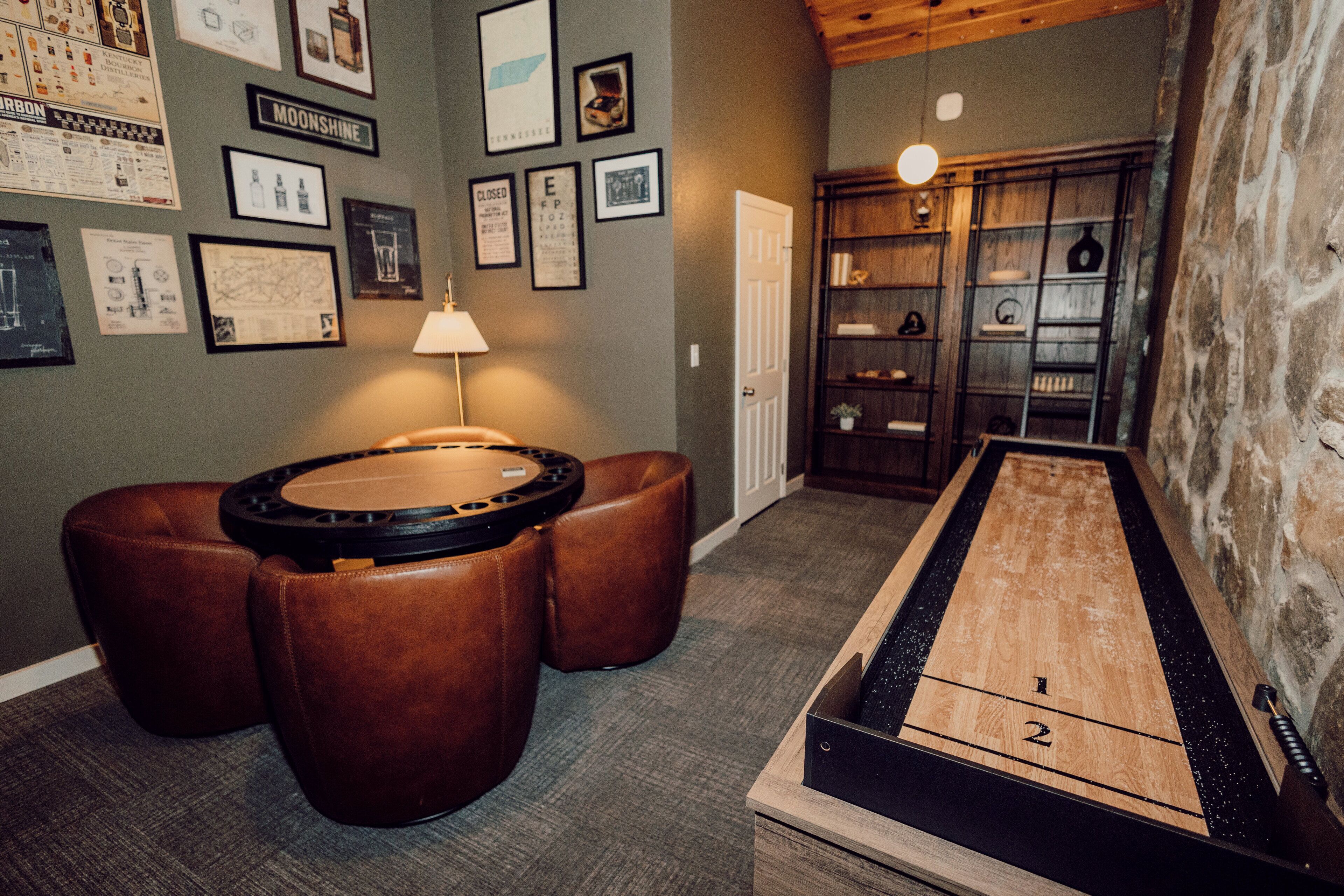 Une table de billard, deux poufs en cuir marron, une lampe et un mur orné de tableaux encadrés.