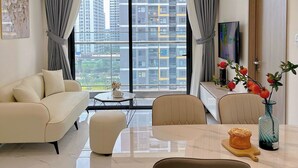 A modern living room with a sofa, dining table, chairs, and a large window with a city view. - Lyshing Apartment in Vinhomes Grand Park (Ho Chi Minh City)