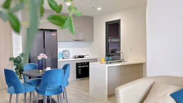 Una sala moderna con un sofá color beige, una mesa redonda y un comedor con sillas azules y un jarrón con flores.