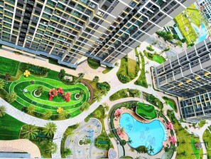 A high-rise residential building with multiple balconies, a landscaped park area with a swimming pool, and a golf course. - Lyshing Apartment in Vinhomes Grand Park (Ho Chi Minh City)