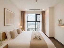 Quarto de hotel com uma cama grande, vista para a cidade, uma obra de arte emoldurada na parede e uma mesa de cabeceira com abajur.