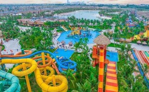 A water park with multiple slides and pools, surrounded by palm trees and a cityscape in the background. - Lyshing Apartment in Vinhomes Grand Park (Ho Chi Minh City)