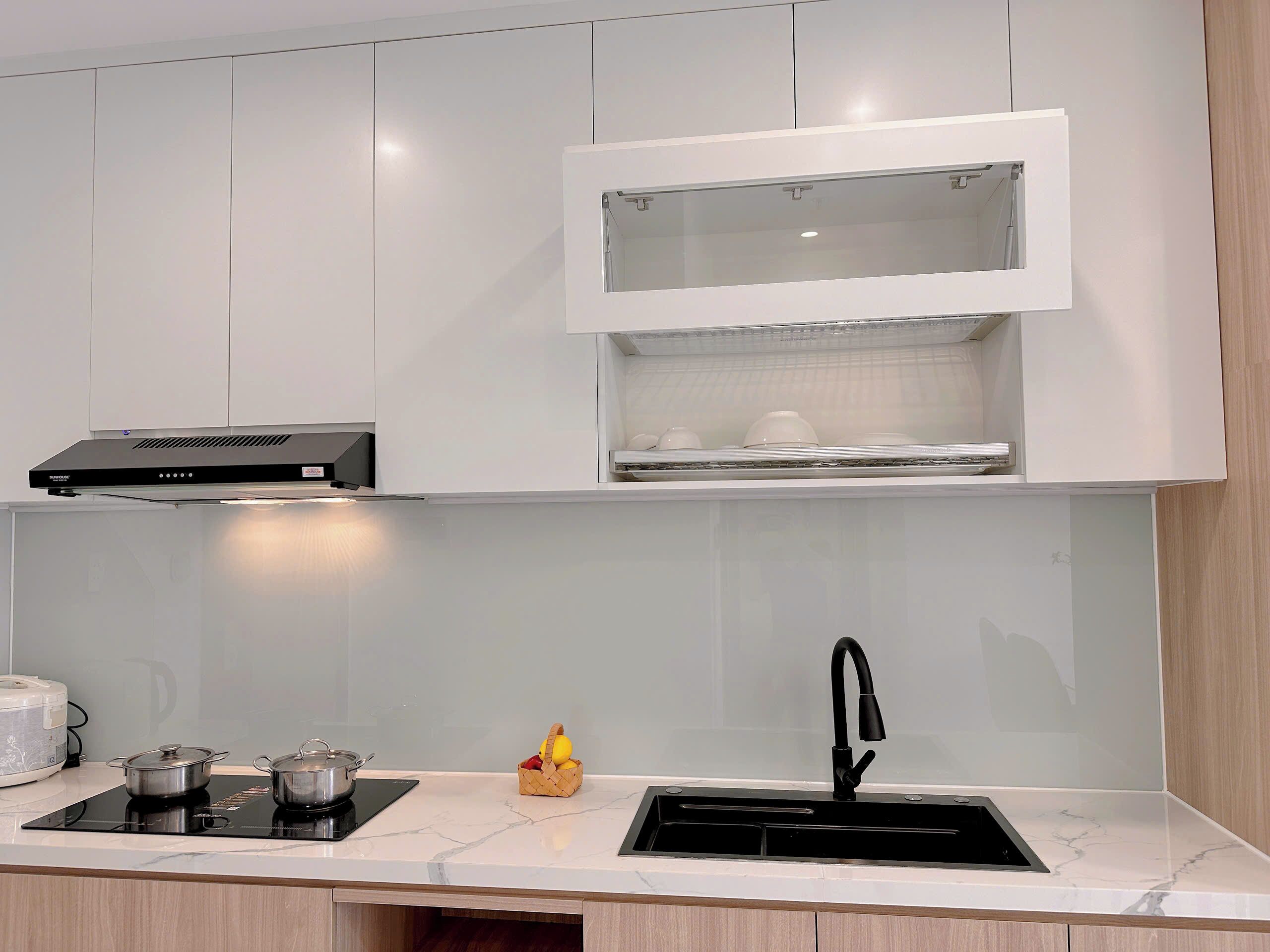 Una cocina moderna con armarios blancos, microondas integrado, grifo negro y una pequeña cesta con frutas.