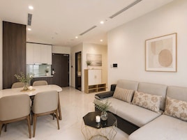 Uma sala de estar moderna com um sofá, uma mesa de jantar com cadeiras, uma mesa de centro e uma área de cozinha ao fundo.