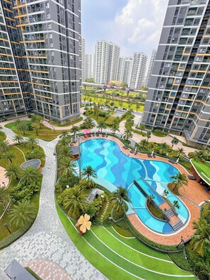A residential complex with a central swimming pool, surrounded by greenery and palm trees. - Lyshing Apartment in Vinhomes Grand Park (Ho Chi Minh City)