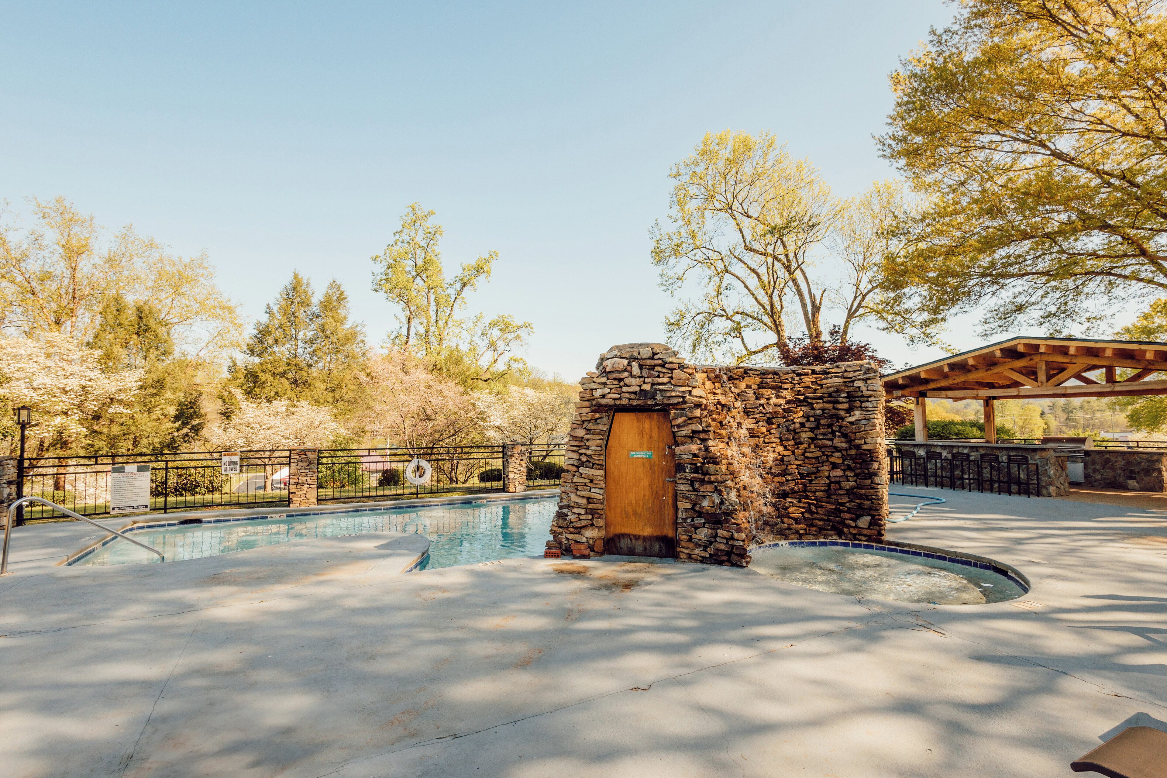 A stone building with a wooden door, a pool, and a covered seating area.