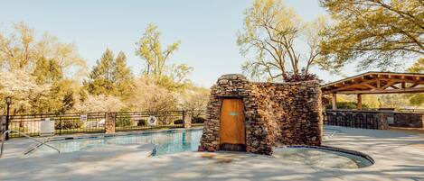 A stone building with a wooden door, a pool, and a covered seating area.