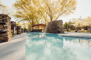Une piscine aux murs en pierre et un pavillon en bois en arrière-plan.