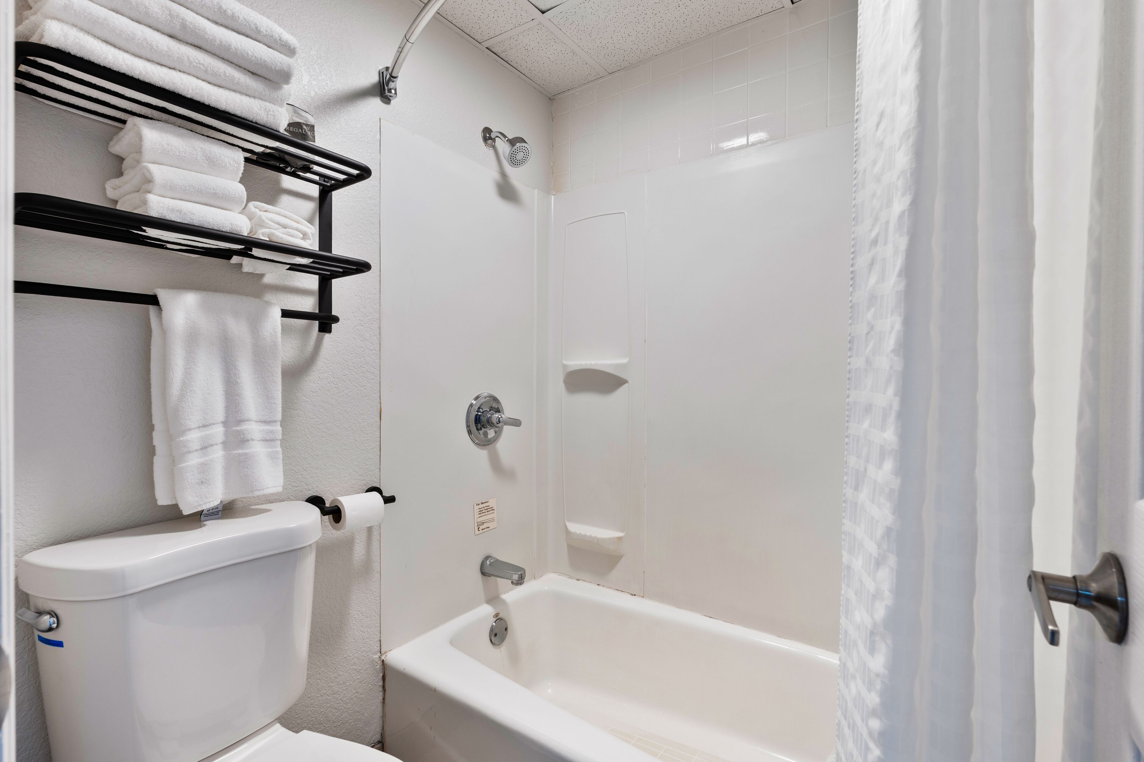 A bathroom with a white toilet, a white bathtub, and a towel rack with folded towels.