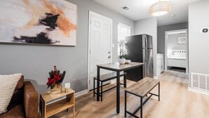 Una cocina moderna con un refrigerador, una mesa de comedor y un banco. Hay un cuadro abstracto grande en la pared y un jarrón con flores sobre la mesa.