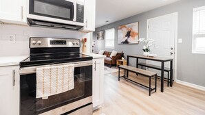 Una cocina moderna con armarios blancos, una estufa negra y un microondas. Hay una zona de comedor con un banco y una mesa.