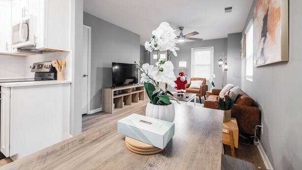 Una sala de estar moderna con una mesa de comedor de madera, un centro de mesa con una orquídea blanca y un sofá marrón.