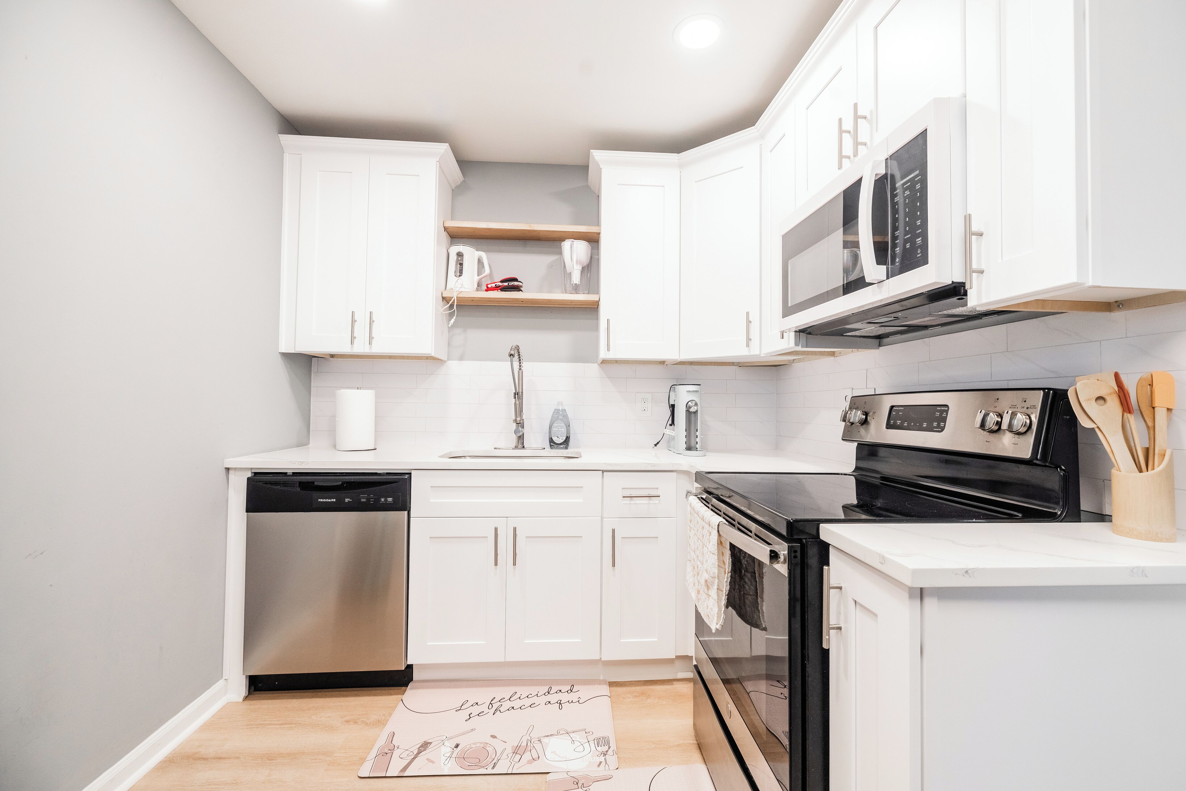 A modern kitchen with white cabinets, a dishwasher, an oven, and a microwave.