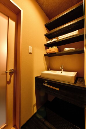 Une salle de bain avec un lavabo blanc, des étagères en bois foncé et une porte en bois.