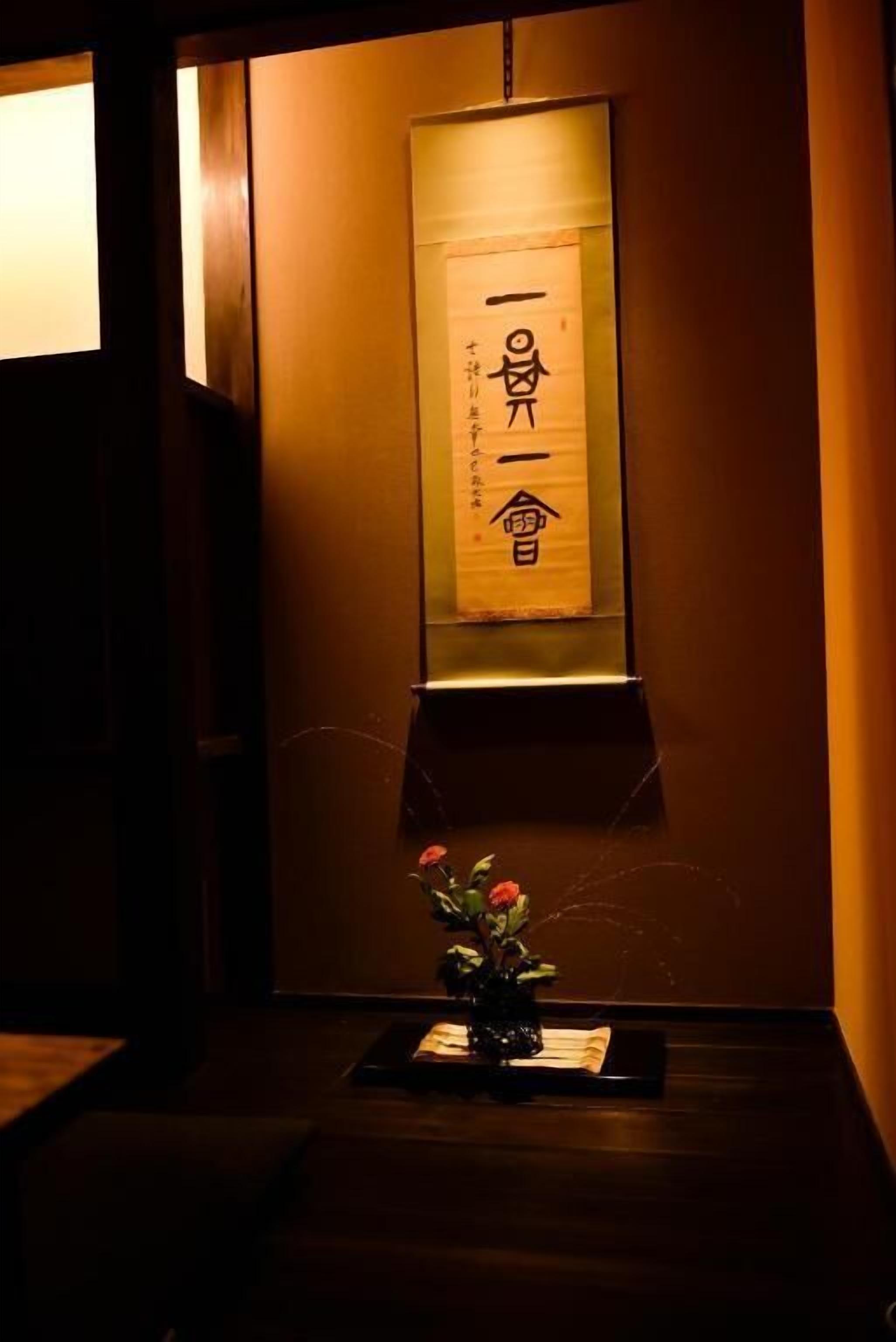 A traditional Japanese room with a sliding door, a wooden floor, and a wall-mounted scroll with calligraphy.