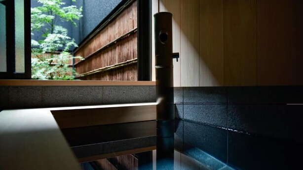 A room with a wooden bench, a black cylindrical object, and a window with a view of greenery. - Miro Hachijo Genmachi BeTei (Kyoto)