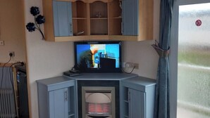A living room with a television, wooden cabinets, a radiator, and a sliding glass door. - 3Bed-Sleeps6-Pet Friendly-FamilyFriendly (Mablethorpe)