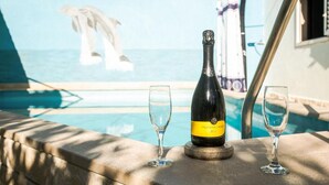 En flaska champagne och två glas på ett bord vid en pool med utsikt över havet.