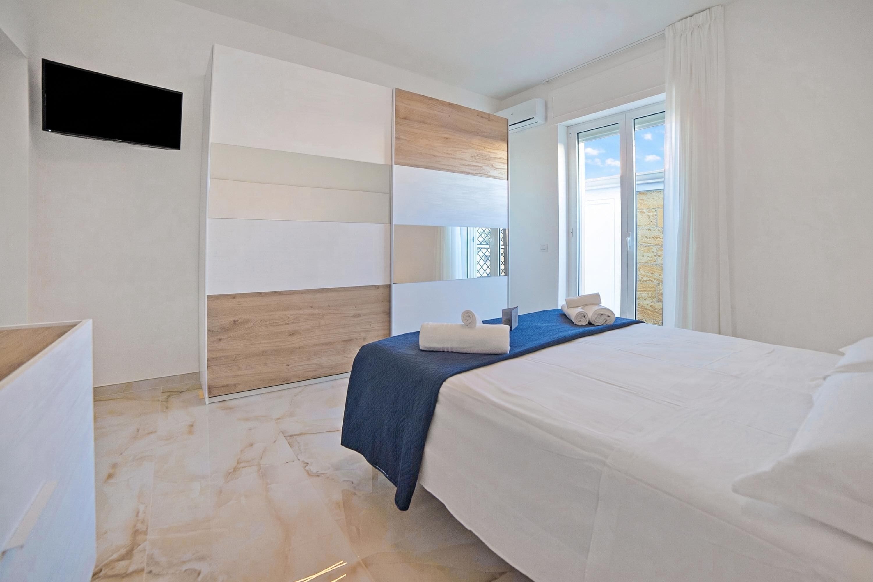 Una habitación de hotel moderna con cama, televisor de pantalla plana, un muro decorativo de madera y una ventana con vistas.