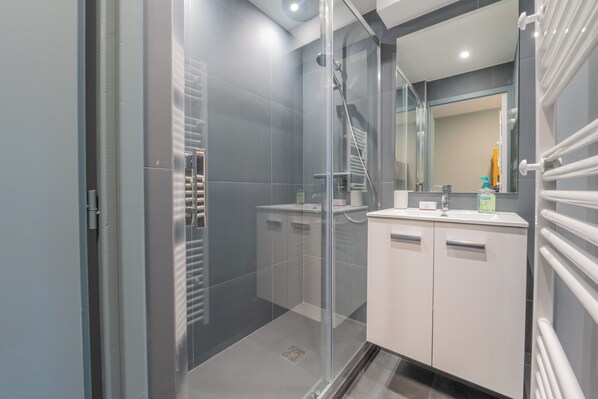 Un baño moderno con cabina de ducha de vidrio, tocador blanco con espejo y perchero.