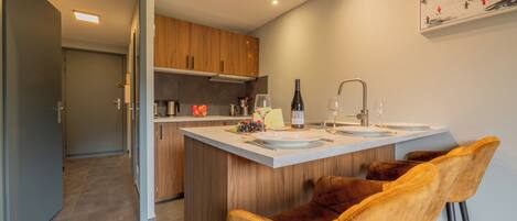 A modern kitchen with a central island, wooden cabinets, and a bar area with two stools.