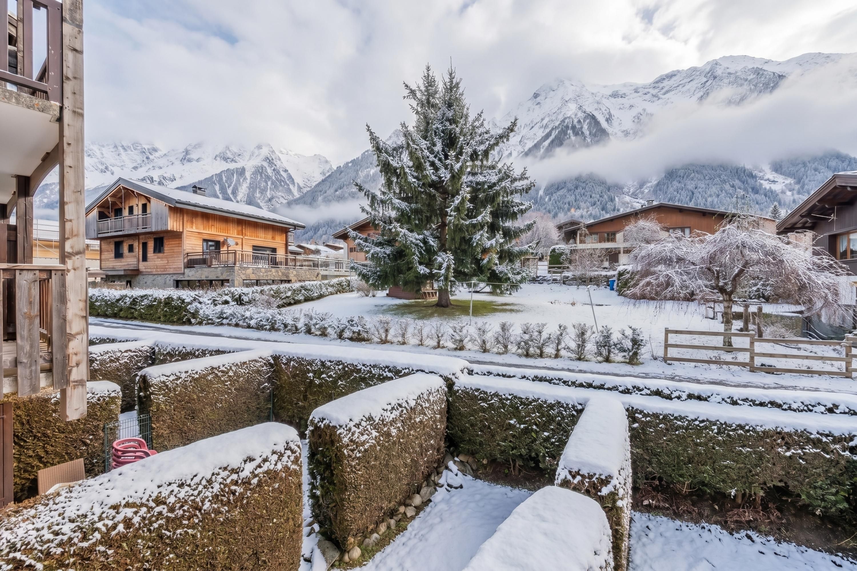 Un pueblo cubierto de nieve en la montaña, con edificios de madera y un abeto grande en el centro.