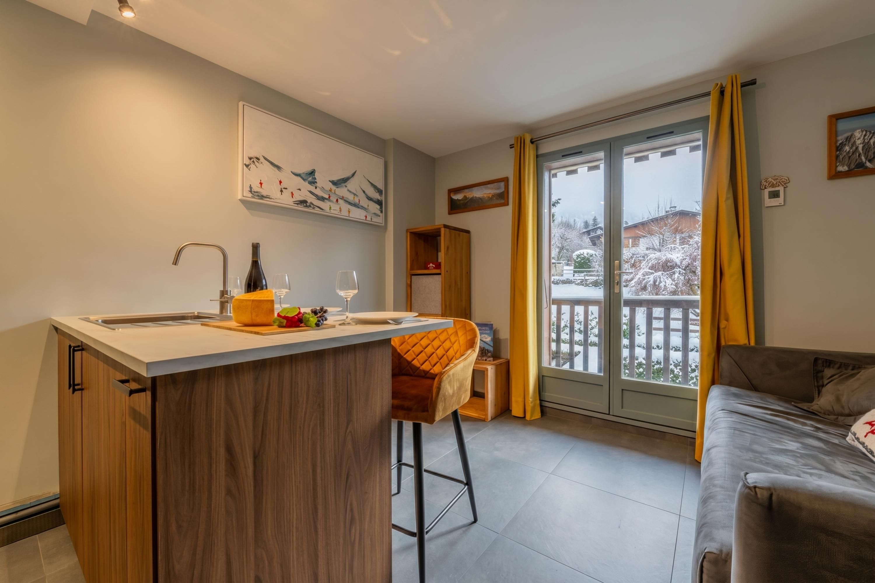 Una cocina moderna con una isla central, una zona de comedor con una silla de madera y vistas a un paisaje nevado a través de un ventanal corredero.