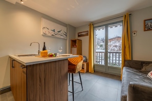 A modern kitchen with a central island, a dining area with a wooden chair, and a view of a snowy landscape through a sliding glass door.
